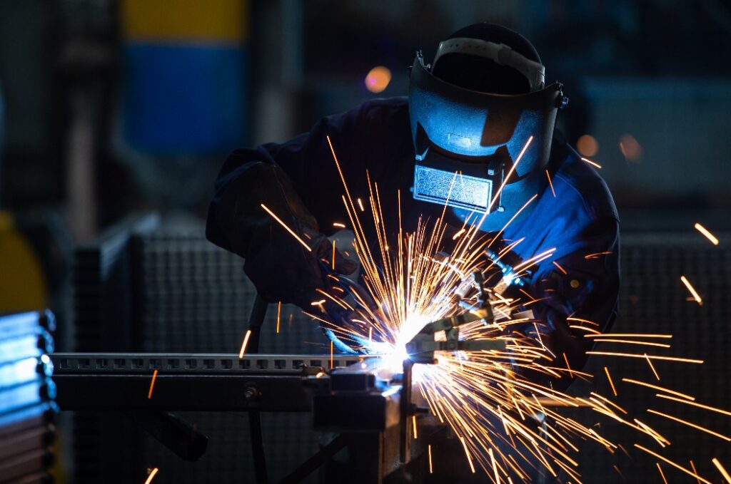 Arbeiter in Industrieuniformen und mit geschweißter Eisenmaske bei Stee
