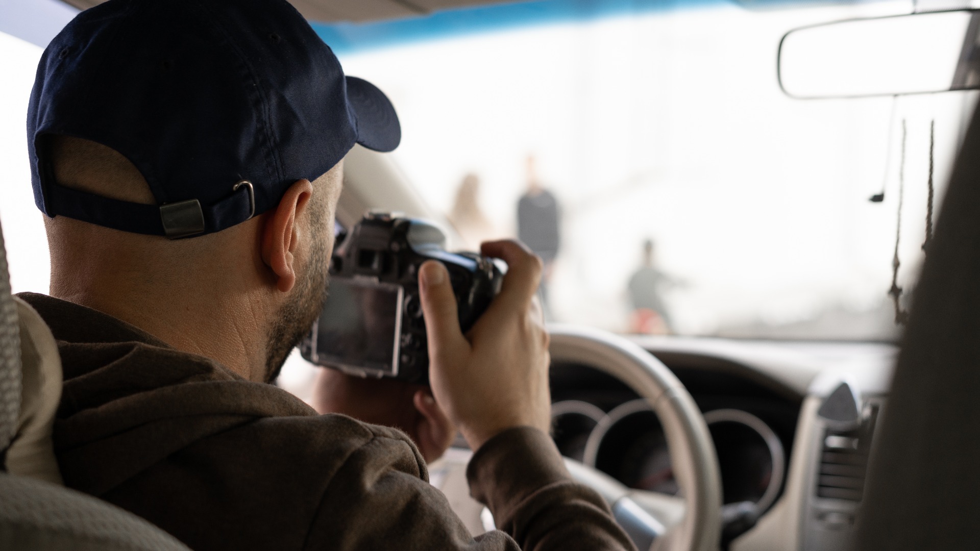 Privatdetektiv, der in einem Fahrzeug sitzt und mit einer Spiegelreflexkamera fotografiert