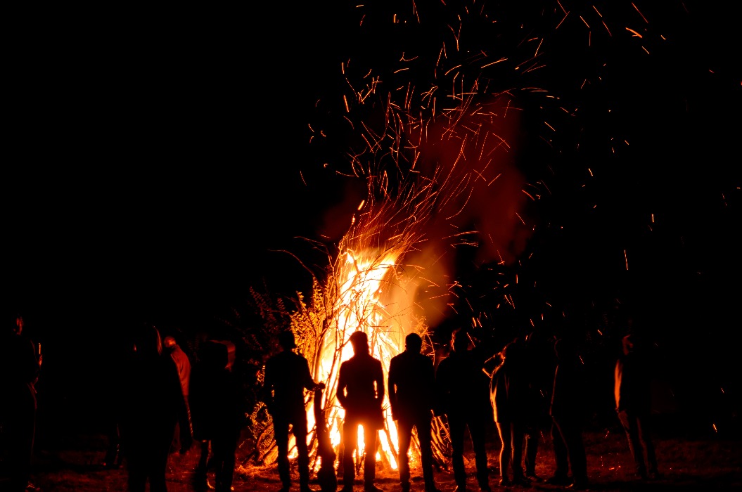 Menschen stehen nachts um ein großes Feuer herum
